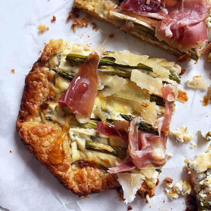 Overhead view of asparagus tart slice with sourdough crust asparagus spears, shaved cheese and prosciutto on parchment