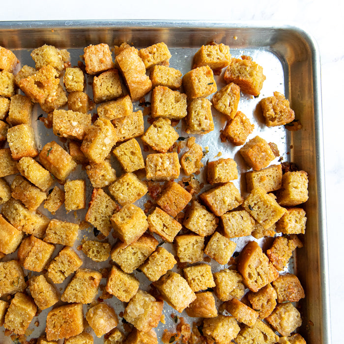Overhead view of herby Einkorn croutons showcasing golden-brown garlicky crisp cubes on a metal baking sheet