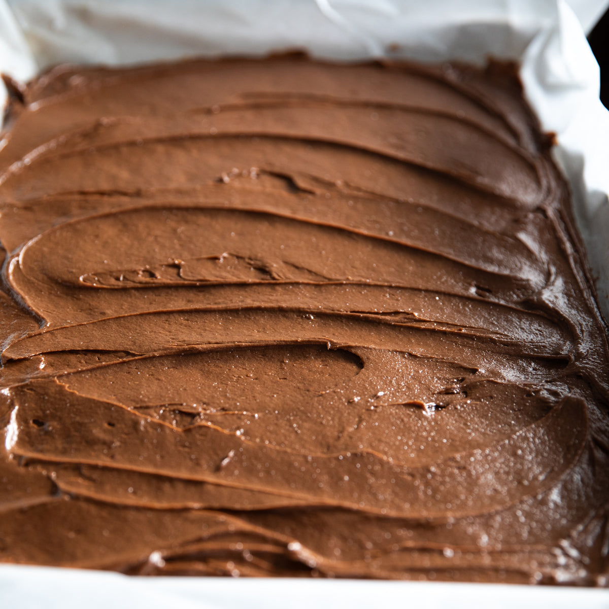 Close-up top view of chocolate ice cream spread in a parchment-lined sheet pan, smooth swirled surface ready for freezing
