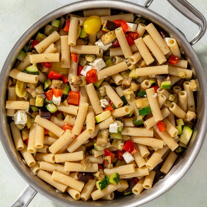 Rigatoni tossed with roasted zucchini, eggplant, red pepper, cherry tomatoes, and feta in a stainless-steel skillet