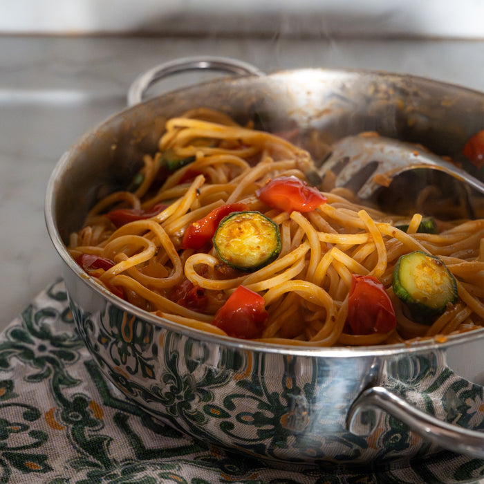 Spaghetti tossed with zucchini and cherry tomatoes in a stainless-steel skillet on a patterned cloth