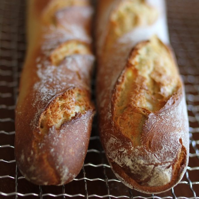 Close-up of two Einkorn French baguettes showcasing crusty golden-brown crust, slashes, and flour dusting on a cooling rack