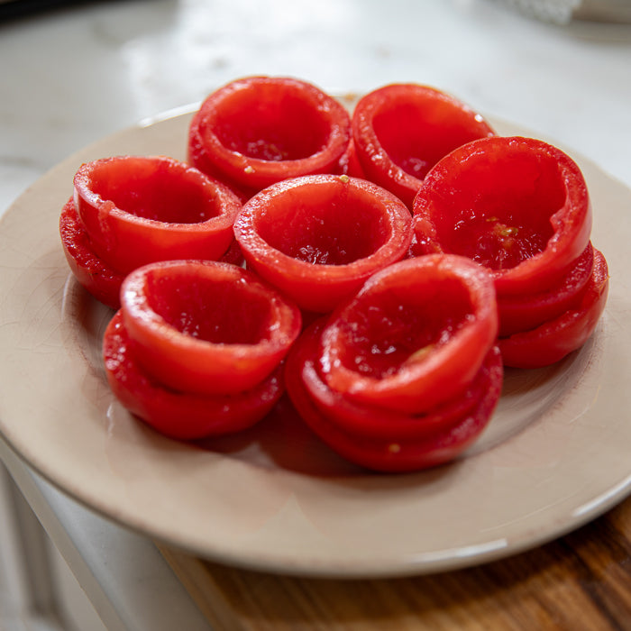 Hollowed ripe tomato halves arranged on a beige plate ready to be filled with einkorn breadcrumb mixture