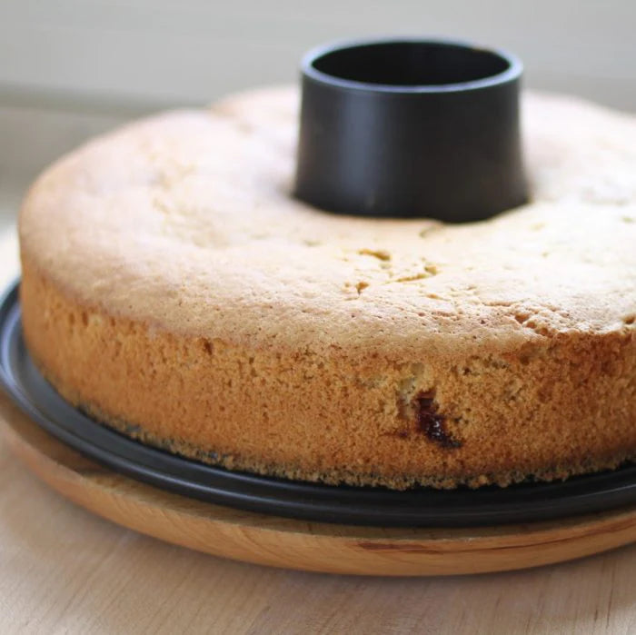 Side view of organic olive oil bundt cake showing light airy crumb and golden-brown crust on black tube pan and wooden board