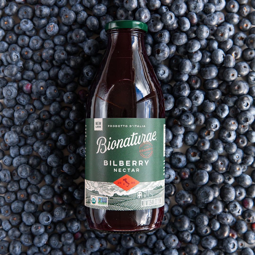 Front view of Organic Fruit Spread Bilberry showcasing the label on a glass bottle with scattered bilberries in the background