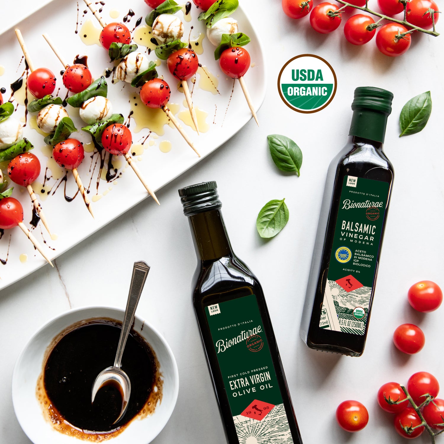 Front view of 17 oz Organic Extra Virgin Olive Oil bottle showing label in dark glass with tomatoes and a bowl of balsamic on a light surface