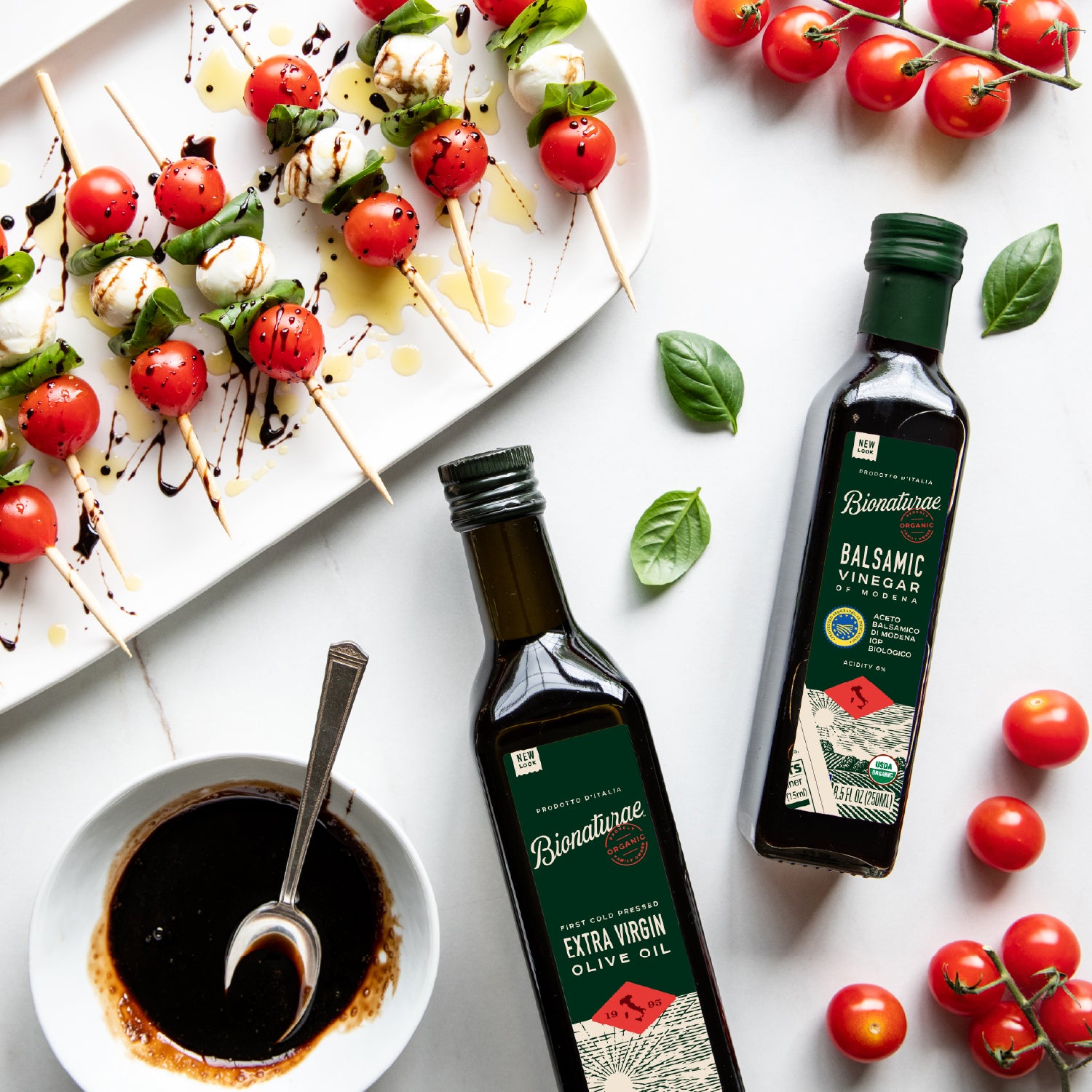 Bottle of Bionaturae organic balsamic vinegar next to a dipping bowl and skewered cherry tomatoes on a white surface