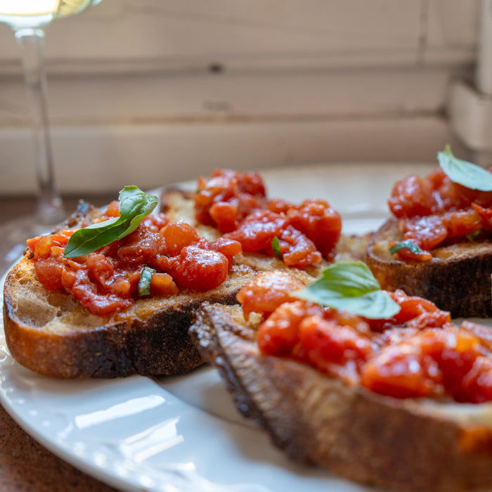 Toasted sourdough slices topped with diced tomato bruschetta and fresh basil on a white plate by a window