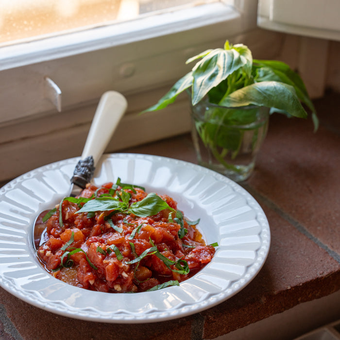 Tomato bruschetta served on a white plate on a sunny windowsill, garnished with fresh basil