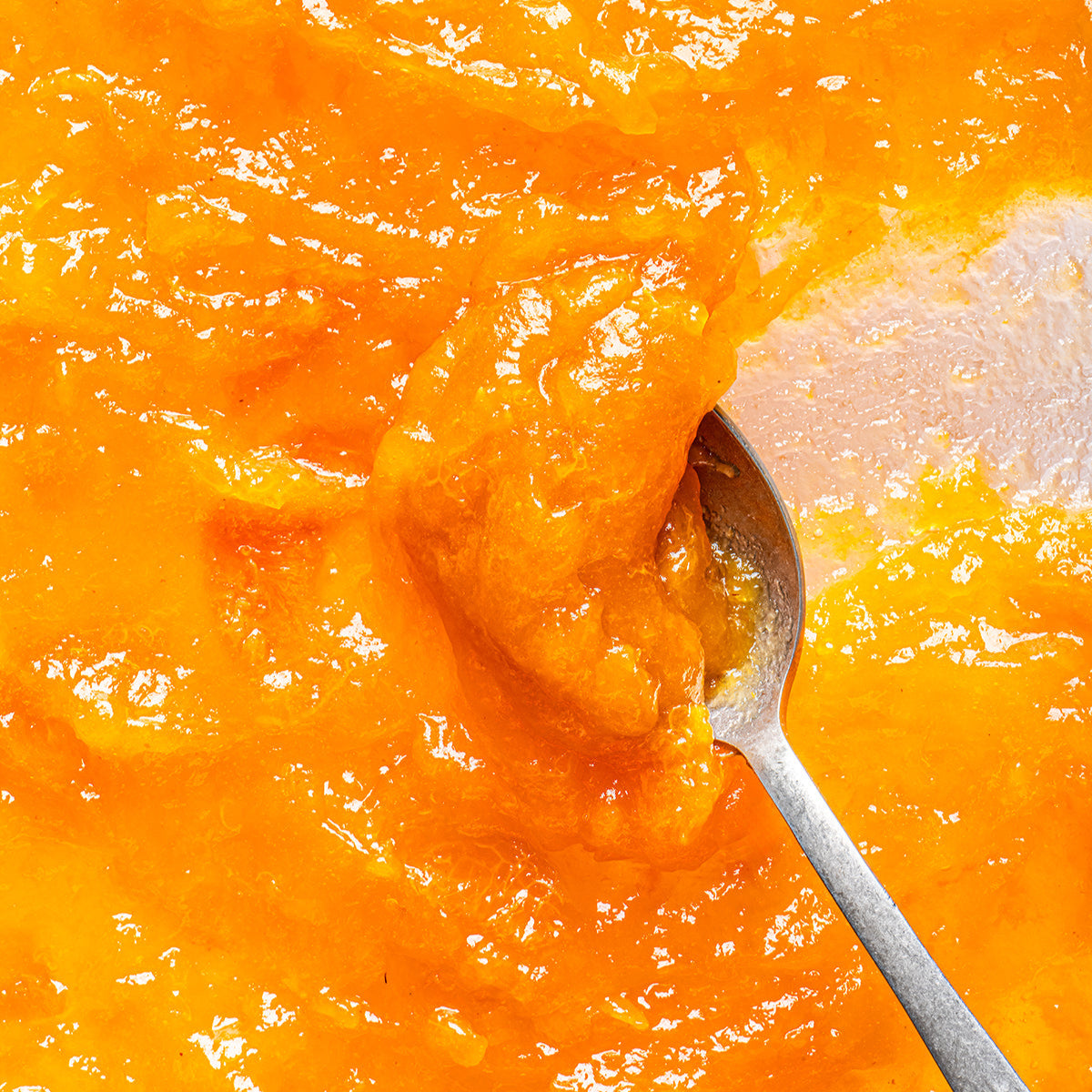 Close-up of Organic Apricot Fruit Spread showcasing glossy orange jam texture on a spoon with a light background