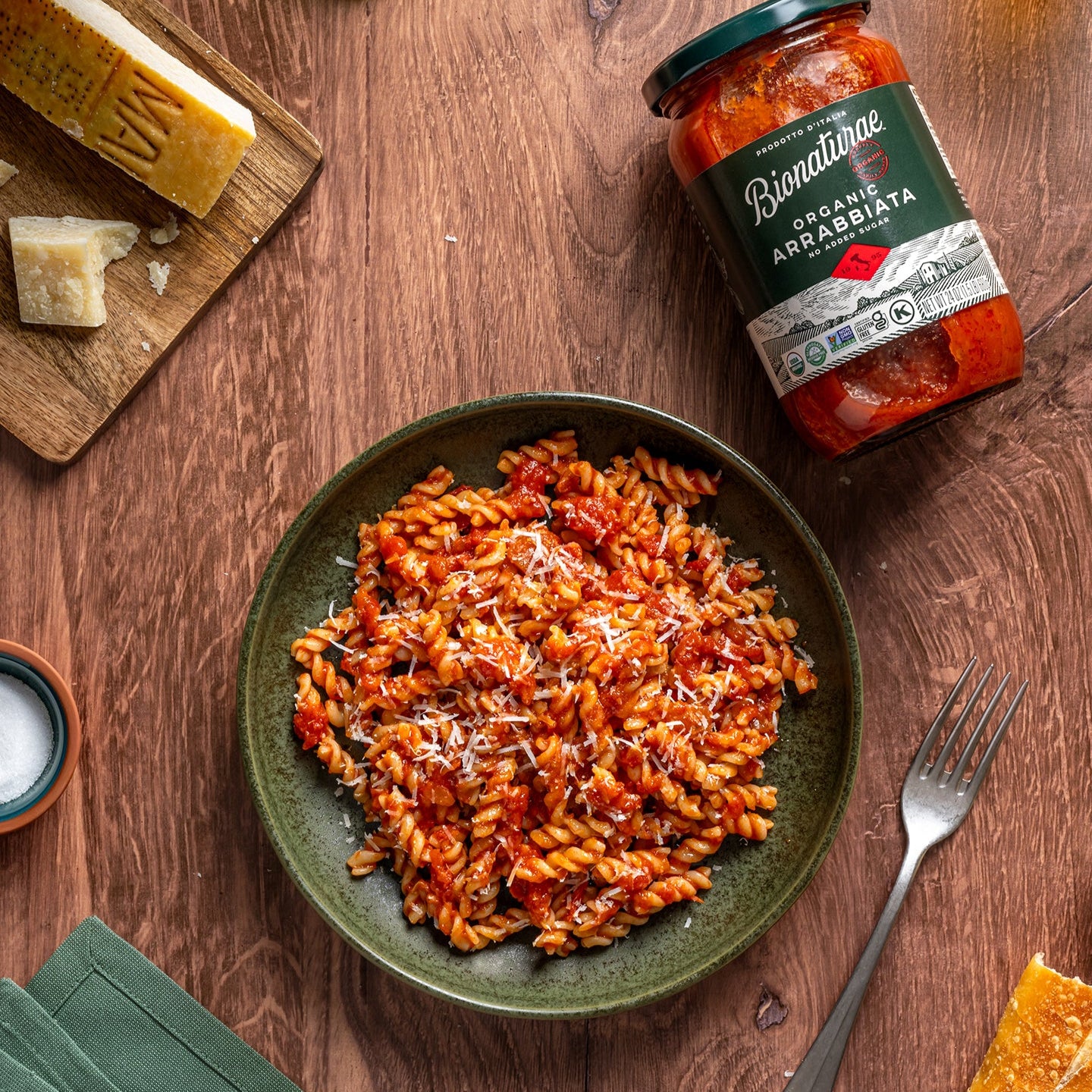 Bowl of cooked organic sourdough fusilli in arrabbiata sauce with a jar of Bionaturae on a wooden table