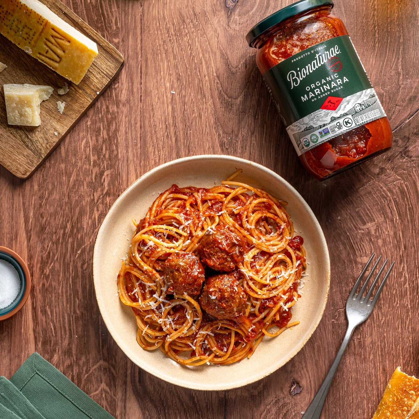 Bionaturae jar of organic marinara sauce beside a bowl of spaghetti and meatballs on a wooden table