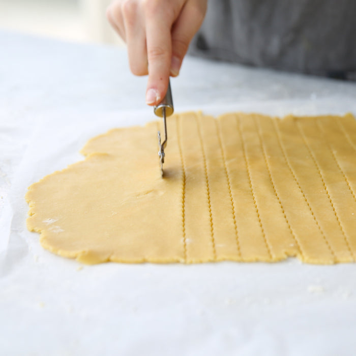 Hand cutting rolled einkorn pie dough into lattice strips with a pastry wheel on a parchment-lined counter