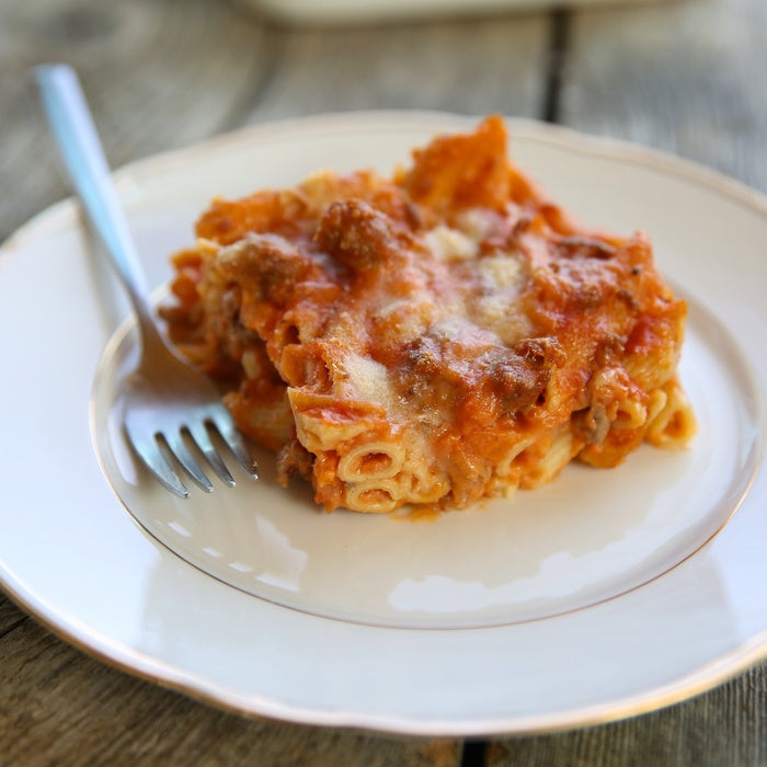 Close-up of penne bolognese pasta bake showcasing browned melted cheese and meat sauce on a white plate with a fork