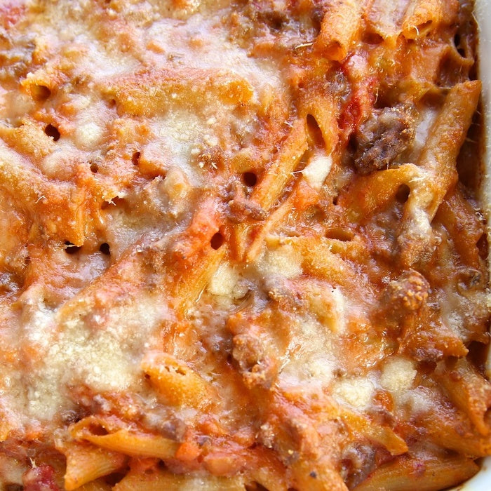 Close-up of gluten-free penne bolognese pasta bake showcasing melted golden cheese and browned meat sauce in a baking dish