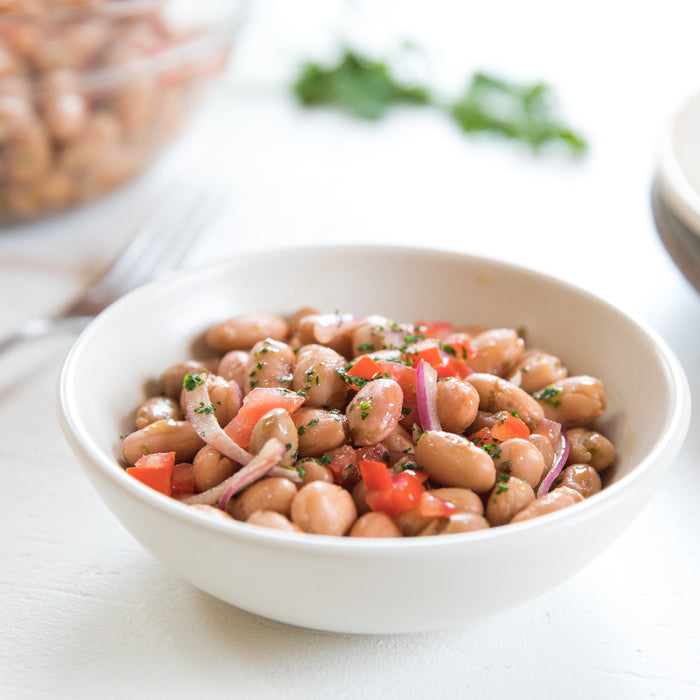 Borlotti bean salad served with chopped tomatoes, red onion, and parsley in a white bowl on a bright surface