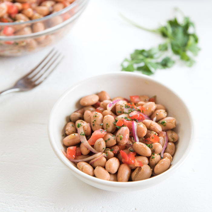 Overhead view of Borlotti bean salad with tomato, red onion, parsley, and olive oil in a white bowl