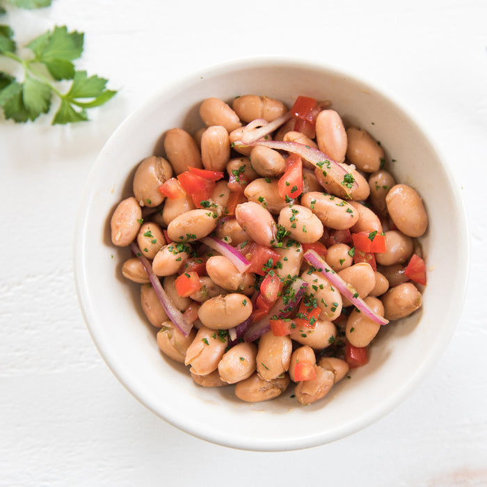 Top-down view of Borlotti bean salad with tomatoes, red onion, and parsley in a white bowl on a white background