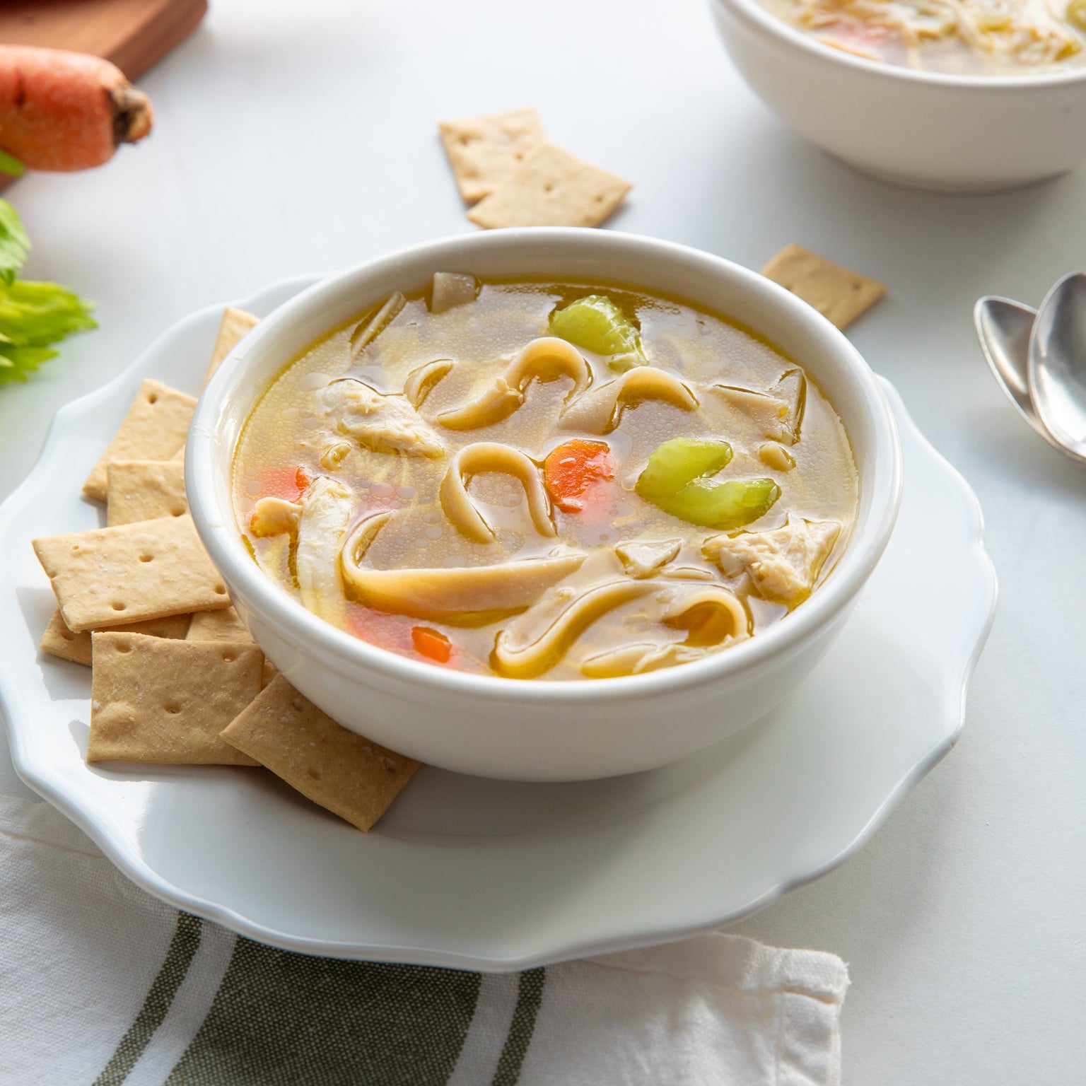 Bowl of chicken noodle soup with gluten-free brown rice egg tagliatelle, carrots and celery, served with crackers