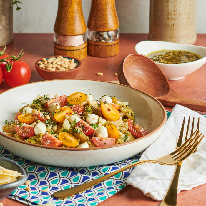 Bowl of Caprese pesto penne with red and yellow cherry tomatoes, fresh mozzarella pearls, pine nuts, and basil