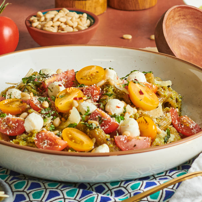 Caprese pesto pasta topped with cherry tomatoes, mini mozzarella balls, pine nuts, and basil on a patterned napkin