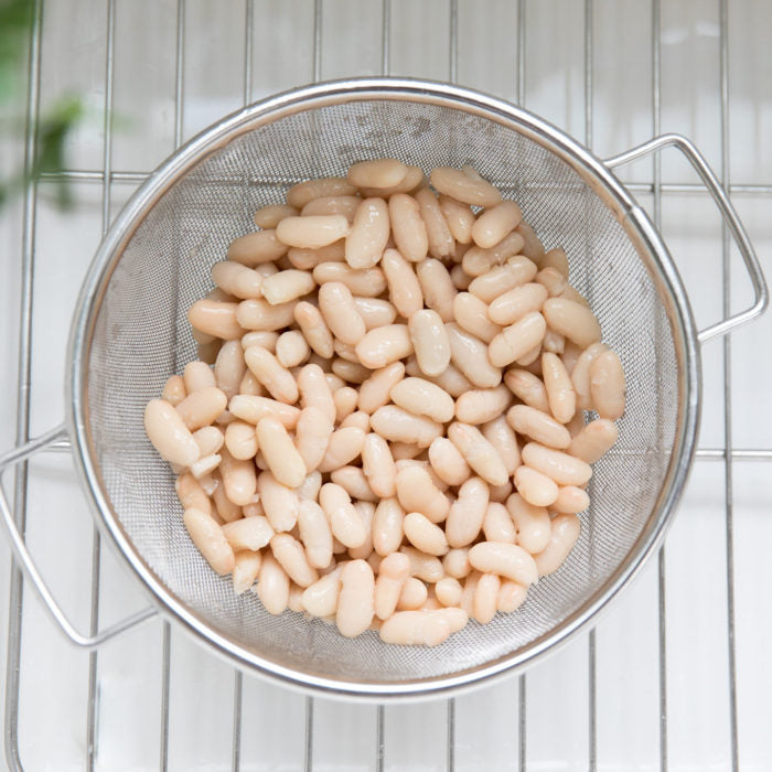 Top view of drained cannellini beans in a stainless steel mesh strainer on a wire rack