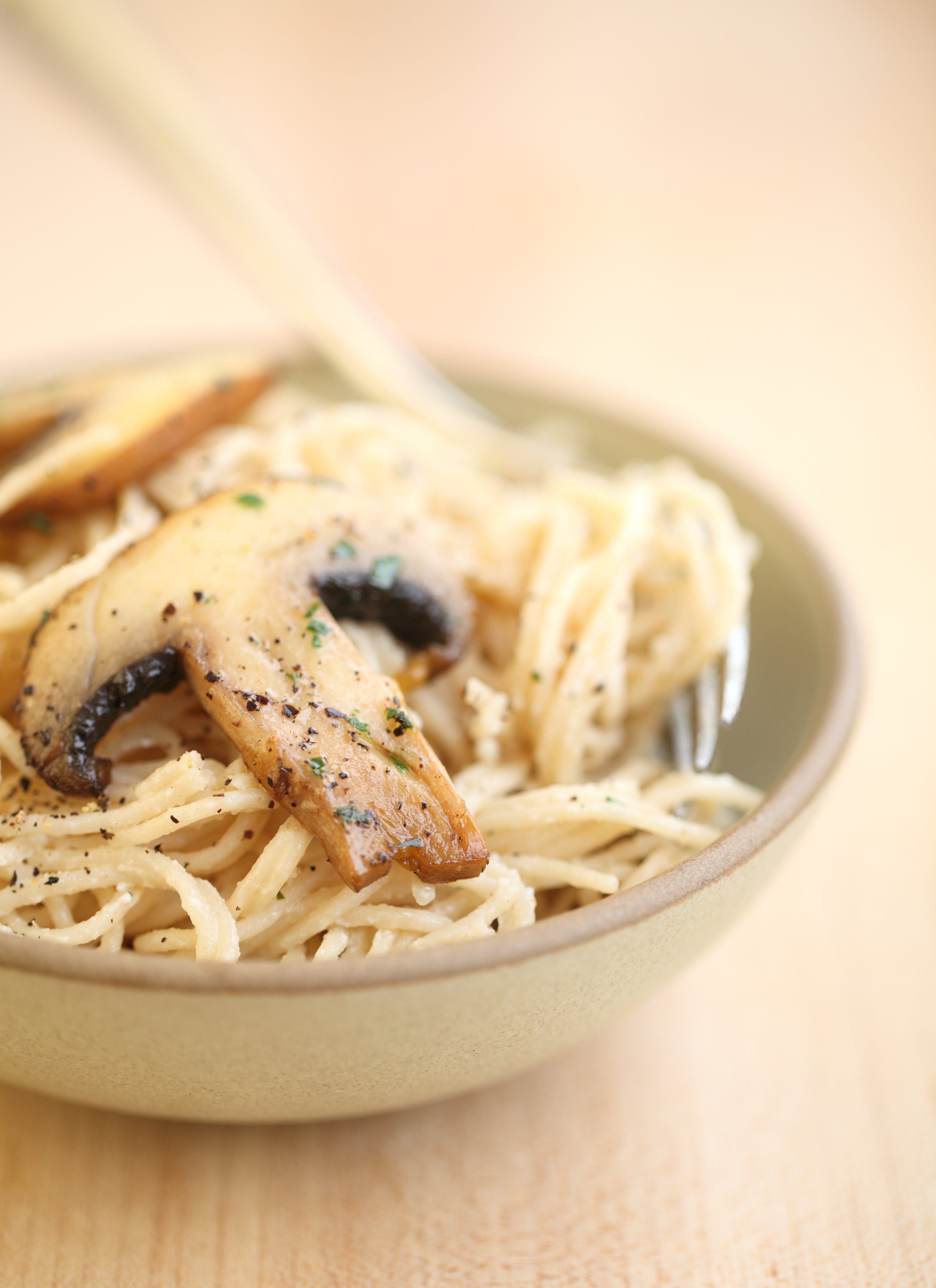 Close-up of capellini with creamy goat cheese sauce and sautéed mushrooms, browned slices on a light wooden table