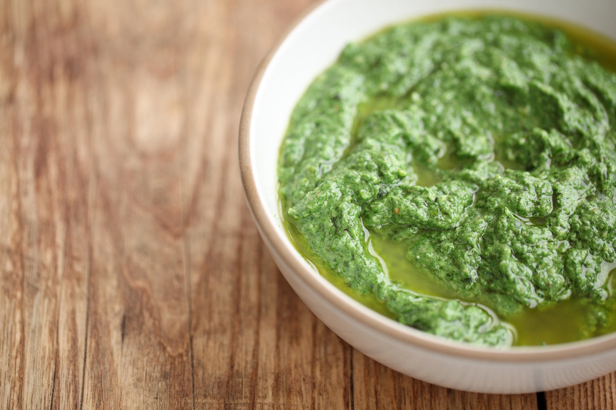 Bowl of spinach basil pesto drizzled with olive oil on a wooden table