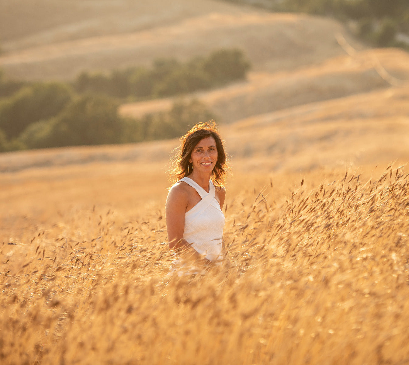 Founder standing in an einkorn wheat field at golden hour, smiling among tall golden stalks
