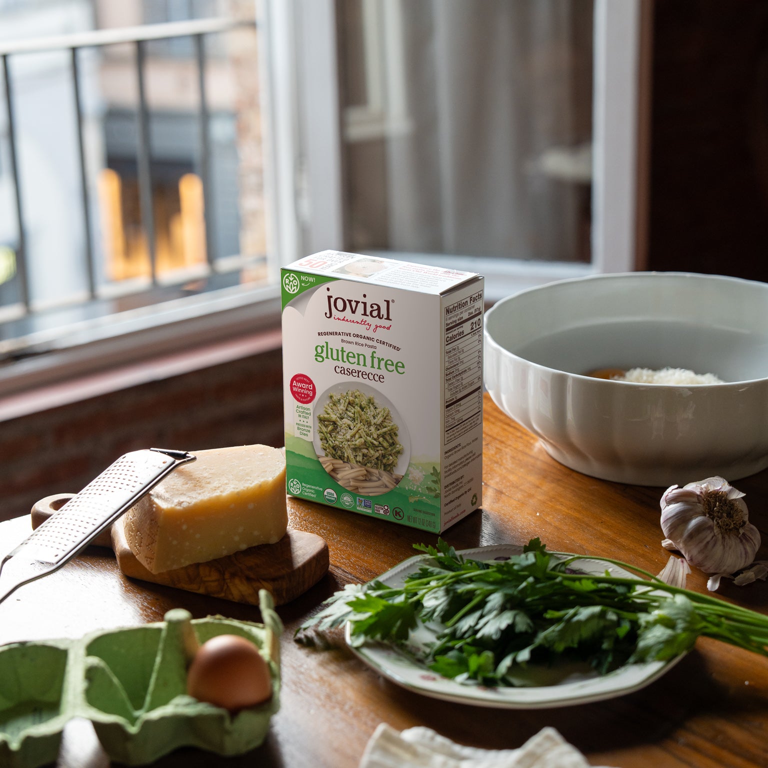 Front view of Jovial gluten free caserecce box on a wooden table with cheese, parsley, garlic, and an egg