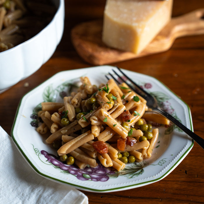 Caserecce pasta in carbonara sauce with peas and pancetta, served on a decorative plate on a wooden table
