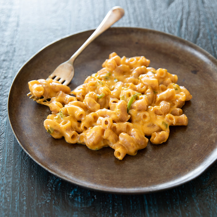 Close-up of gluten-free mac and cheese on a dark plate with creamy cheddar-style sauce and green chiles
