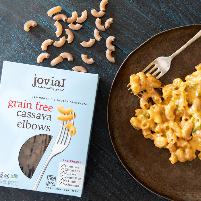 Top view of Jovial grain free cassava elbows box with fork graphic and a plate of creamy mac and cheese on a dark table