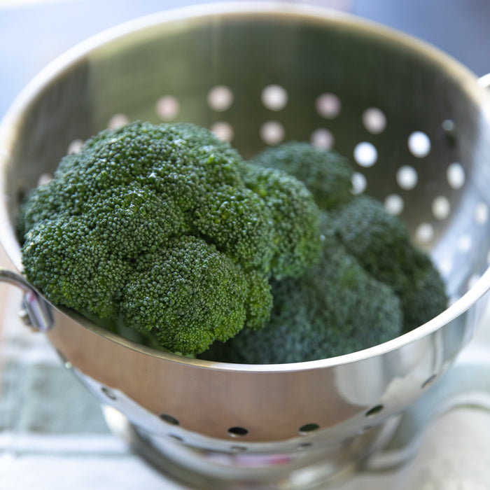 Close-up of broccoli florets in a stainless steel colander showing fresh dark green texture with soft kitchen background