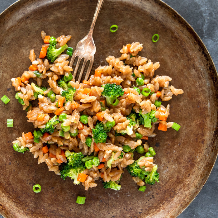 Gluten-free Jovial cassava orzo fried rice with broccoli, peas, carrots, and scallions served in a brown bowl with a fork