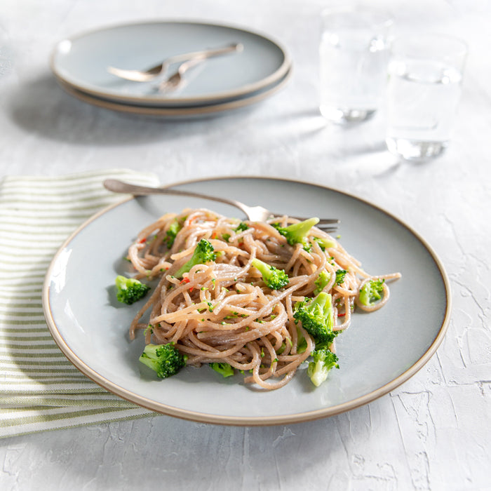 Plate of gluten-free spaghetti tossed with garlic, olive oil, chili flakes, and broccoli on a grey plate