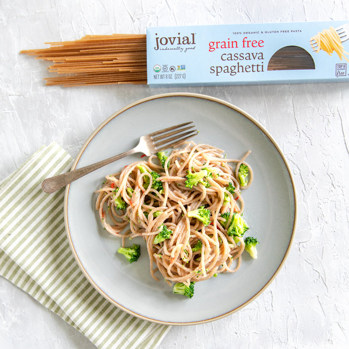 Plate of cassava spaghetti with broccoli and garlic, fork on plate, Jovial grain-free cassava spaghetti box at top
