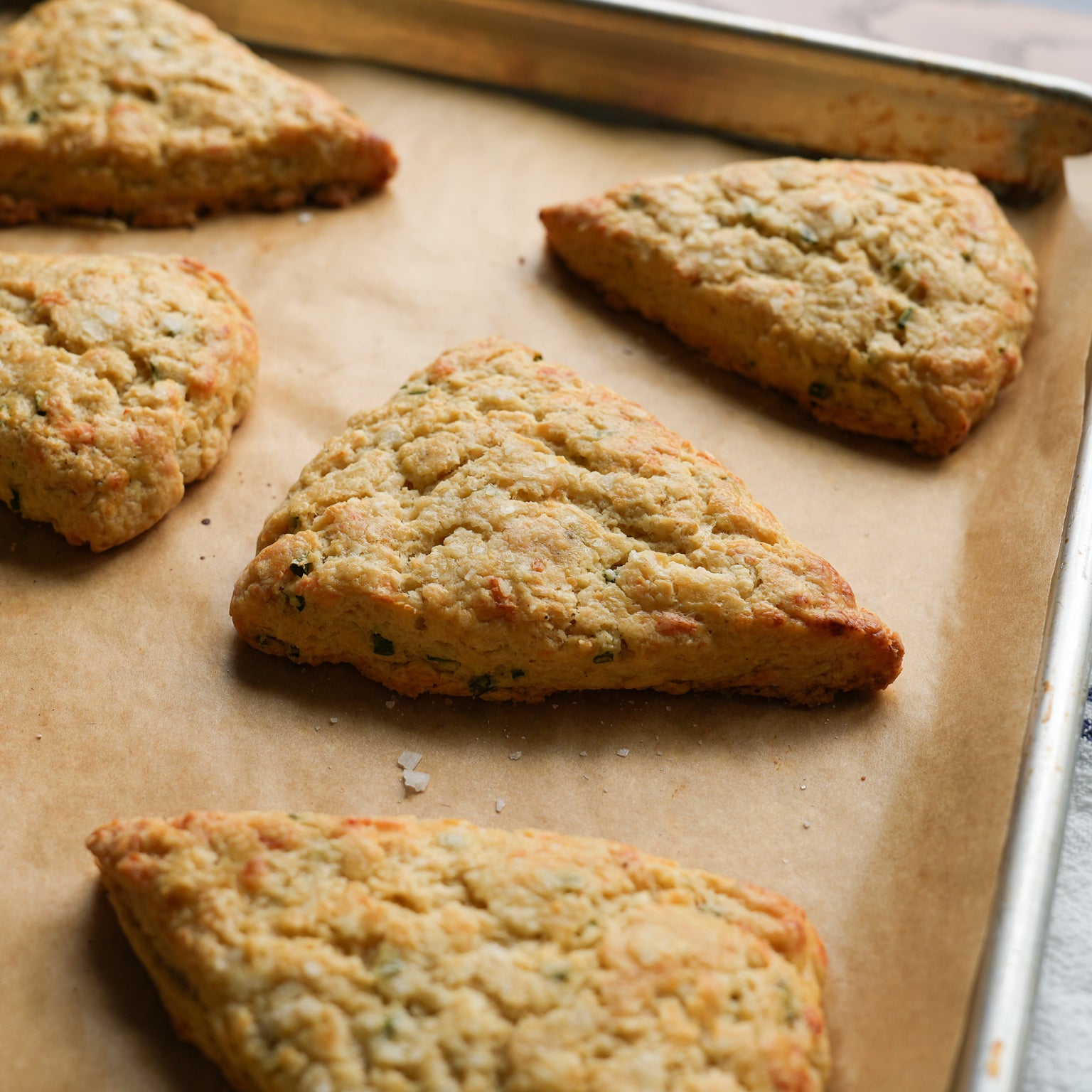 Close-up of cheddar and chive einkorn scones on parchment-lined baking sheet showing golden flaky texture