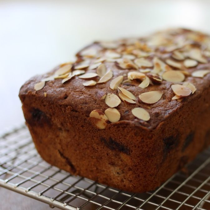 Close-up of Einkorn cherry almond quick bread with sliced almonds on top and cherries, on a wire cooling rack