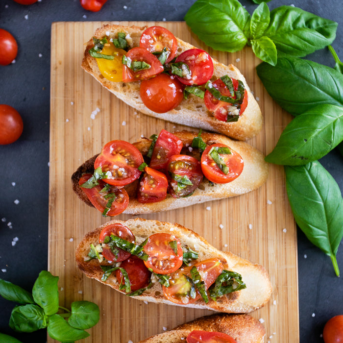 Italian cherry tomato bruschetta on toasted baguette slices arranged on a wooden board with fresh basil and sea salt