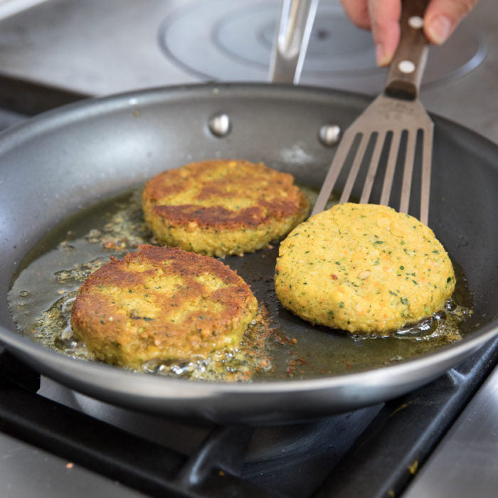 Three chickpea veggie burgers frying in a skillet, one being flipped with a metal spatula