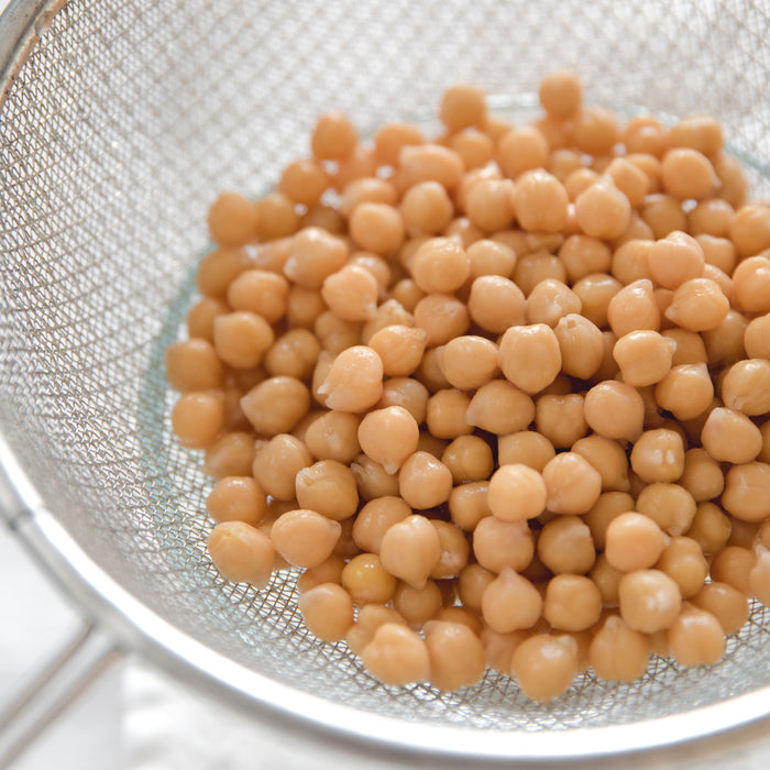 Close-up of cooked chickpeas in a metal strainer showcasing smooth, glossy texture on white background