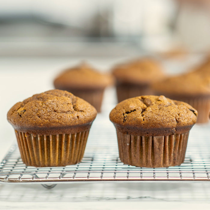 Front view of two Einkorn pumpkin chocolate chip muffins on a cooling rack with golden-brown tops and paper liners