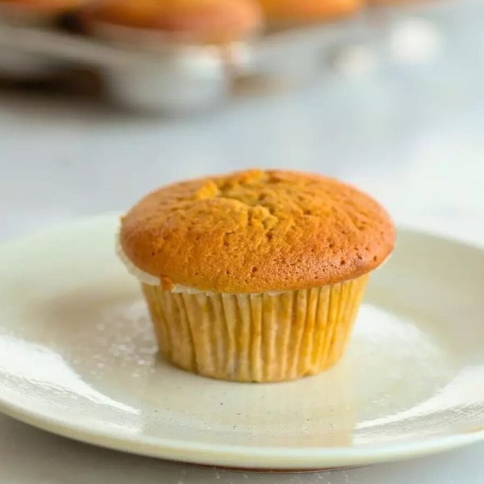 Front view of an Einkorn pumpkin muffin showcasing a golden-brown domed top and paper liner on a white plate