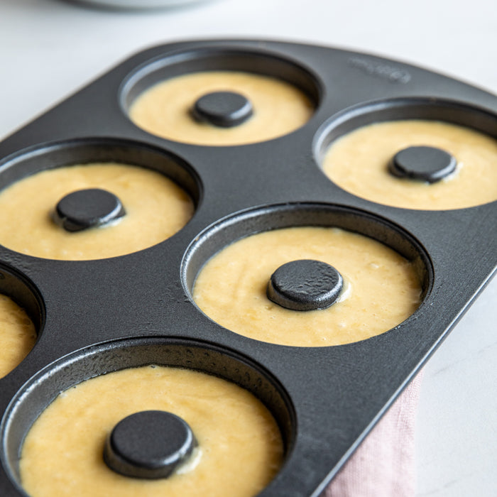 Einkorn donut batter filling a nonstick donut pan on a light countertop
