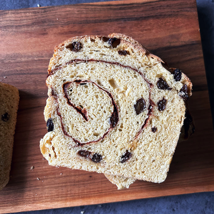 Top view of a slice of Einkorn sourdough cinnamon raisin loaf with cinnamon swirl and raisins on a wooden cutting board