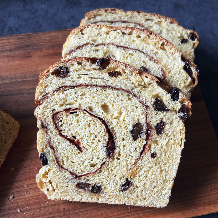 Close-up of sliced Einkorn sourdough cinnamon raisin loaf showing cinnamon swirl and raisins on a wooden cutting board