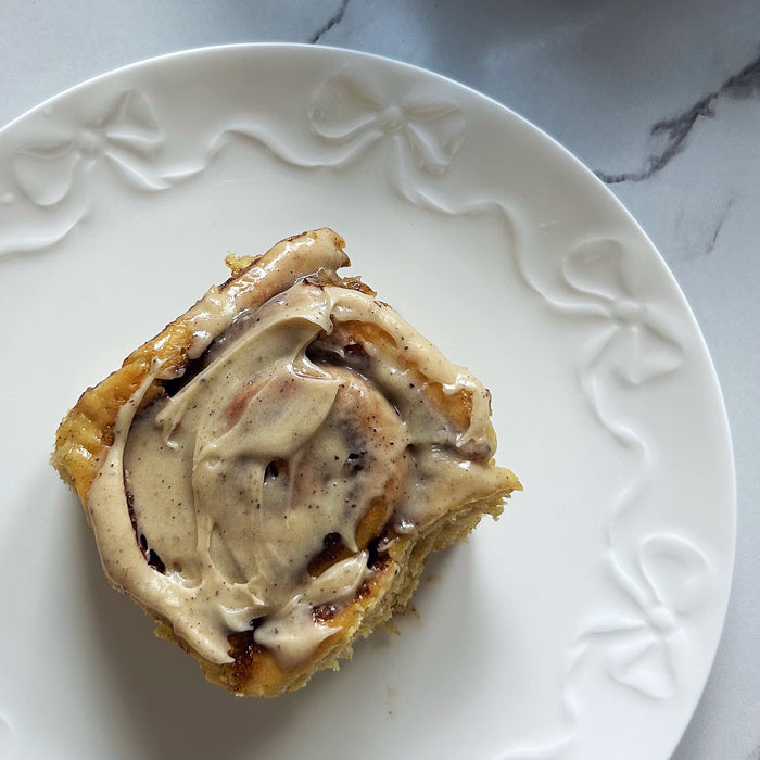 Top-down view of sourdough cinnamon roll with cream cheese glaze and visible cinnamon swirls on white embossed plate over marble surface
