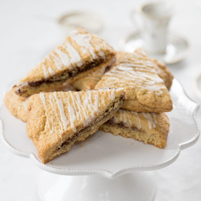 Close-up of Einkorn cinnamon scones with cinnamon swirl and icing drizzle on a white cake stand