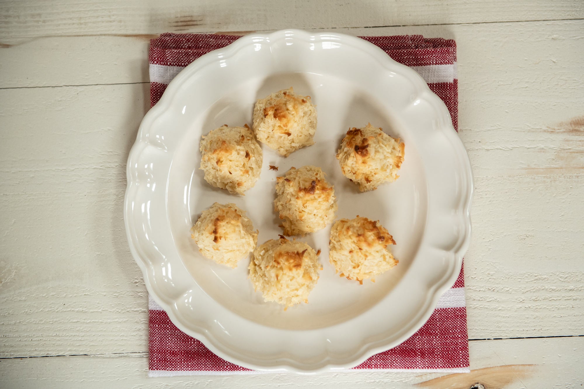 Top-down view of seven vegan coconut macaroons on a white scalloped plate resting on a red-striped napkin